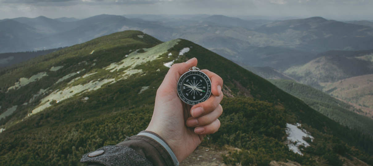 A compass being held in front of a scenic mountain view