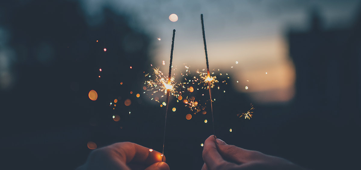 Two lit sparklers held by two hands